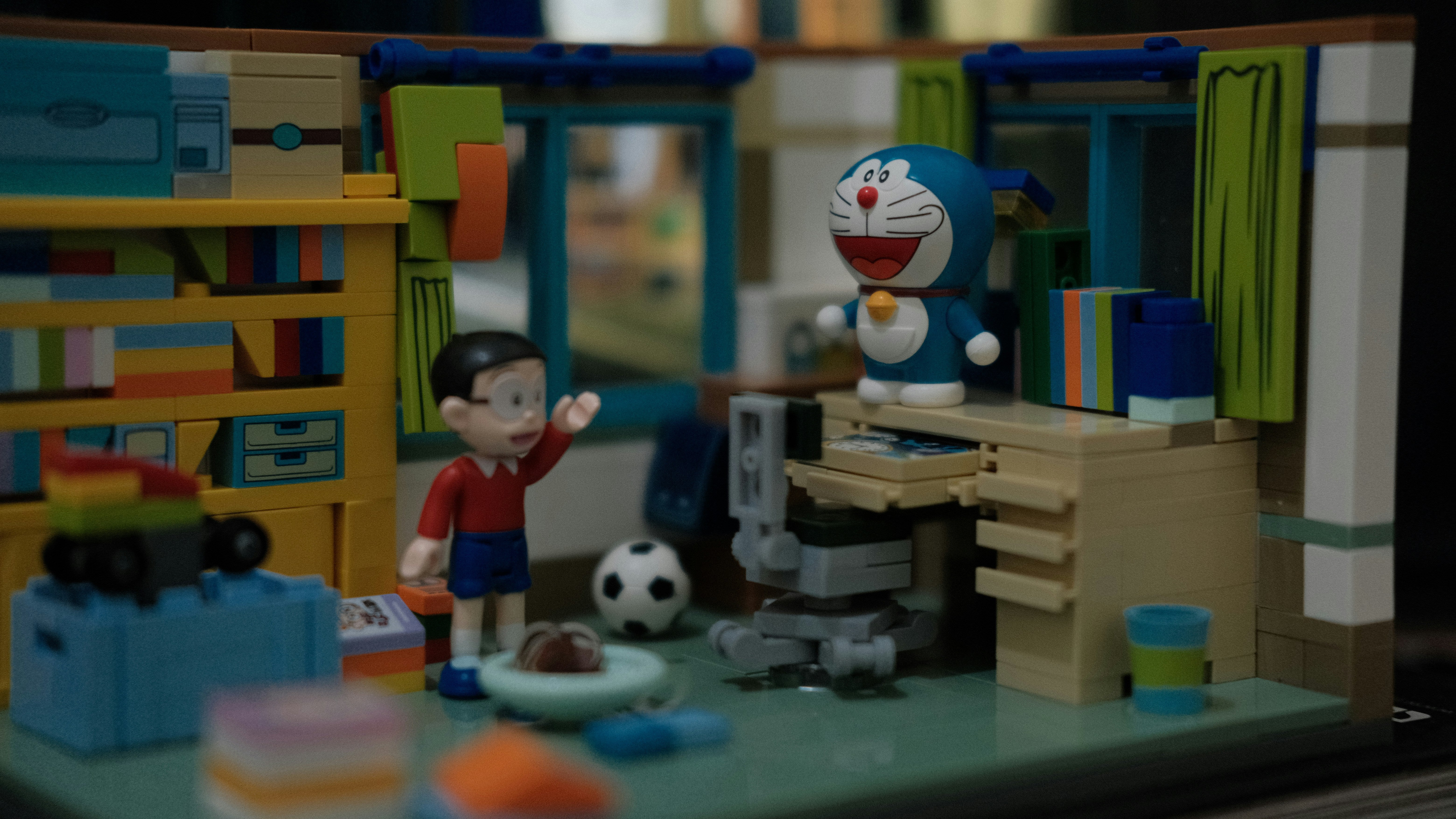 Diorama featuring Doraemon standing on a desk and Nobita beside a football, set in a miniature bedroom scene, representing childhood nostalgia in toy collecting.