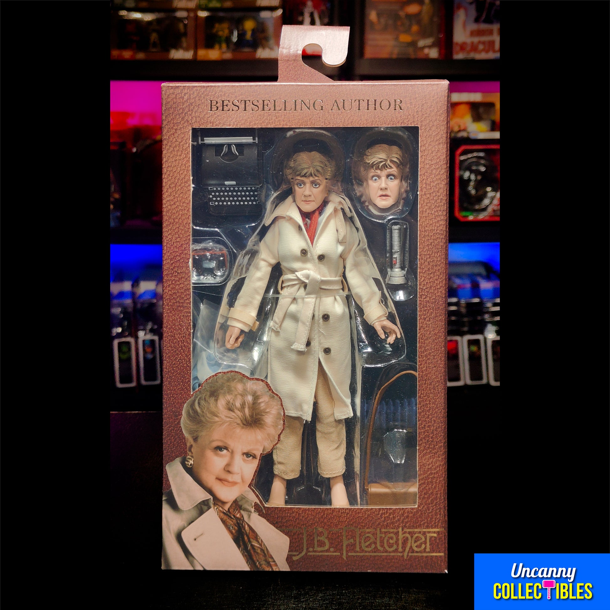 oxed NECA retro-style 8-inch action figure of Jessica Fletcher from Murder, She Wrote, featuring a cloth trench coat, alternate head, typewriter, and accessories, displayed against a collector shelf background.