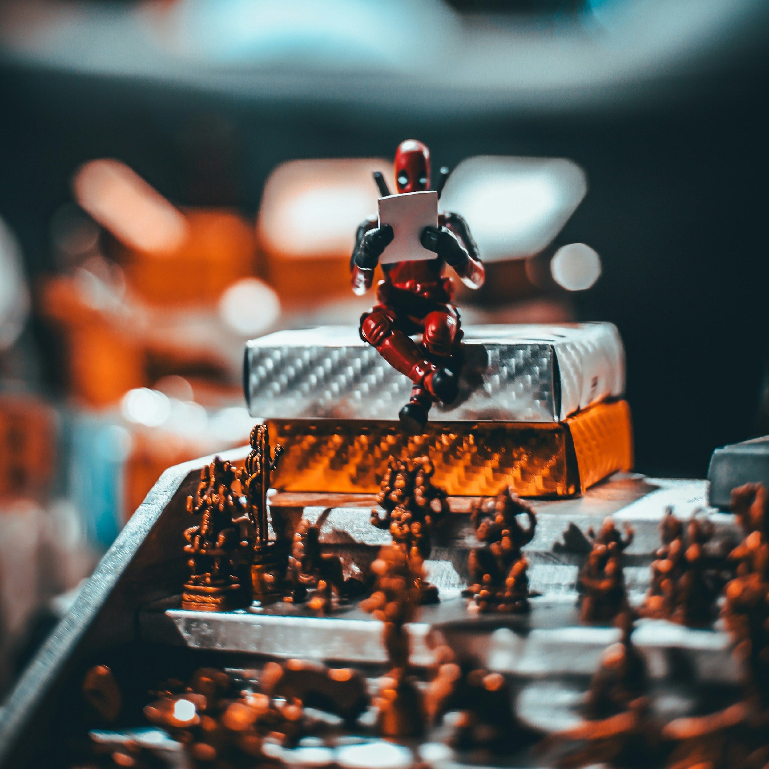 Deadpool action figure sitting on a box, writing on a clipboard with chess pieces below, representing the step-by-step process of selling toy collections.