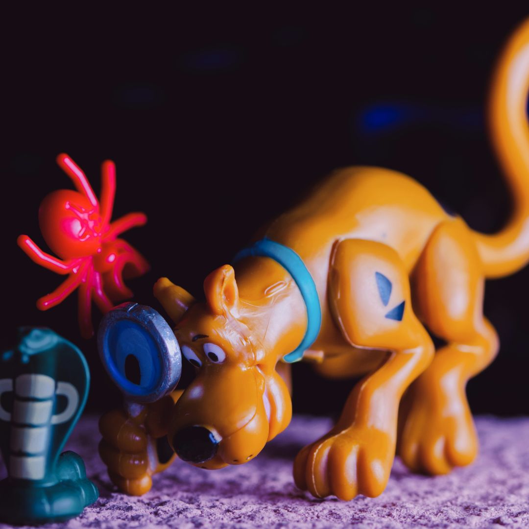 Scooby-Doo action figure crouching with a magnifying glass next to a plastic spider and snake, symbolising detailed research when preparing a toy inventory.