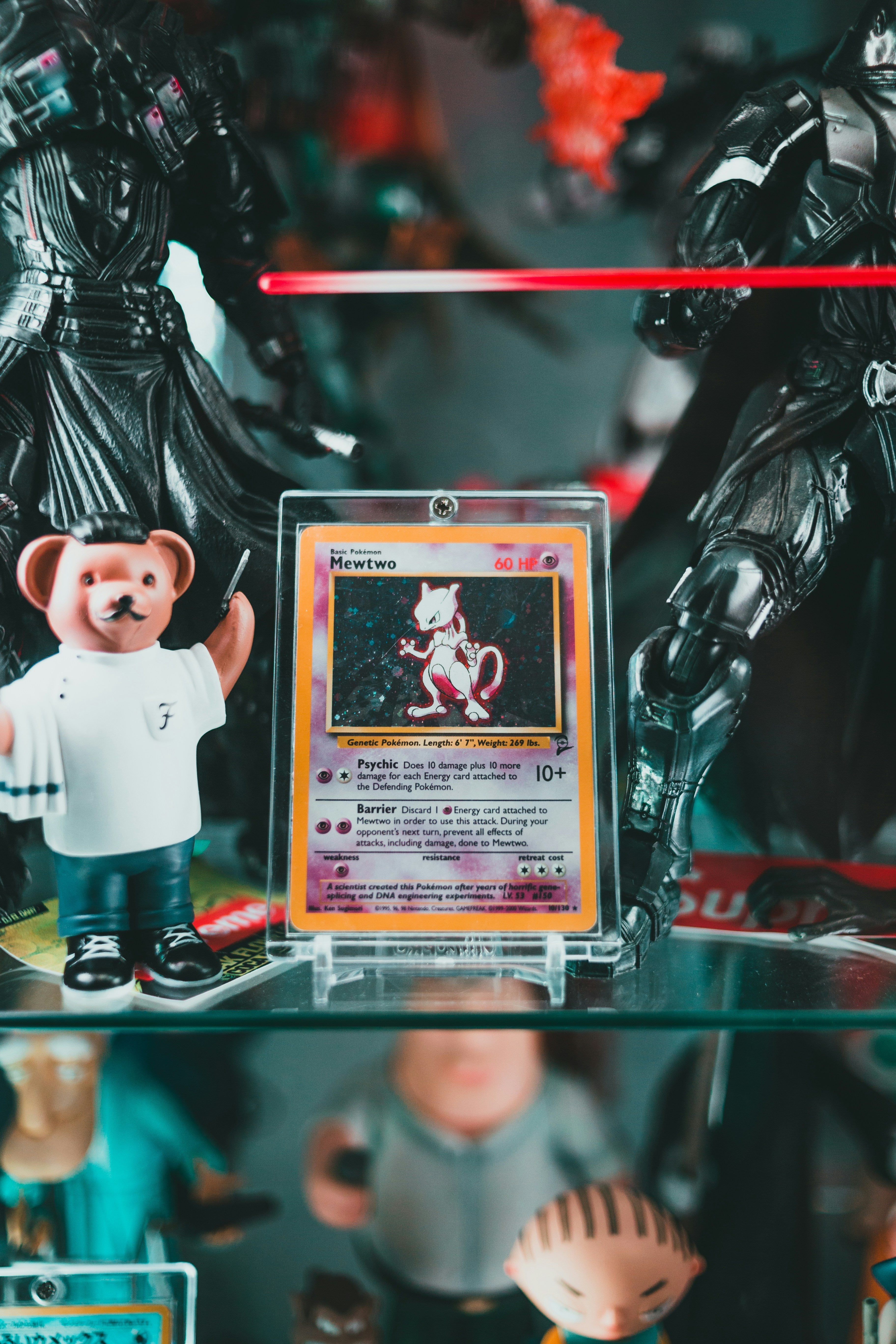 Close-up of a holographic Mewtwo Pokémon card in a protective case on a shelf surrounded by action figures, showcasing collectible condition and rarity.